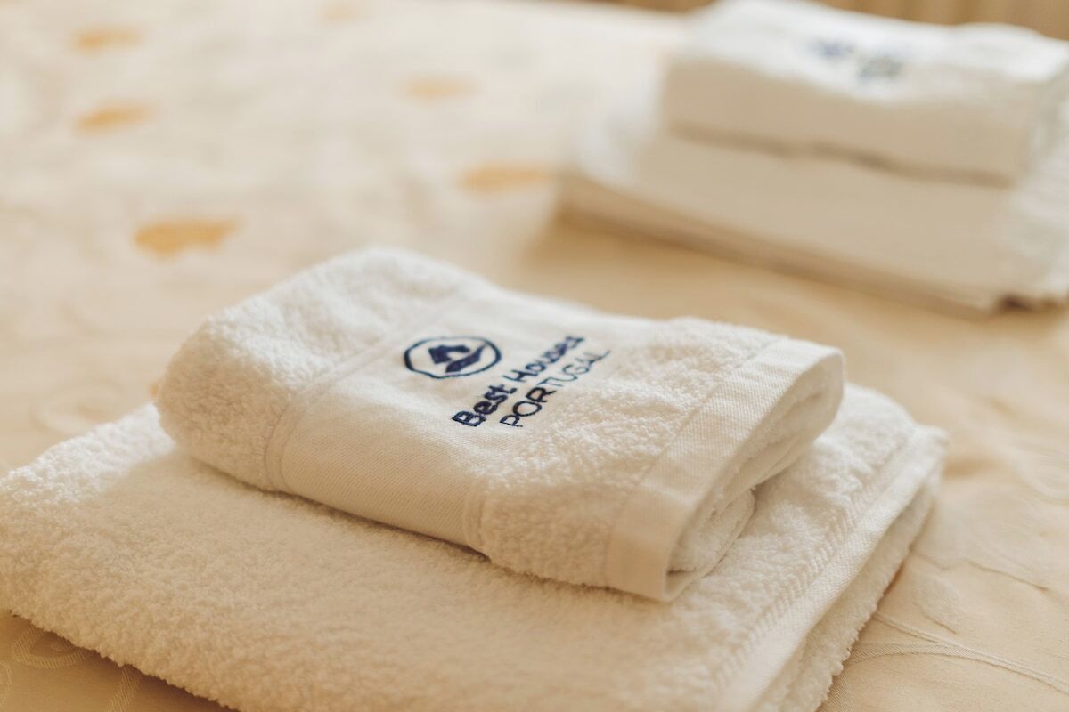 Toallas blancas dobladas con pulcritud, con un logo y texto, sobre una cama.