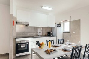 Una cocina moderna con armarios blancos, horno empotrado y comedor con mesa para dos.