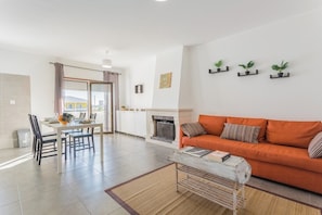 Un salon moderne comprenant un canapé, une table à manger, des chaises, une cheminée et trois plantes en pot disposées sur le mur.