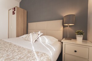 Un dormitorio con cama, mesita de noche, lámpara, planta en maceta y armario.