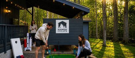 Un espace dédié au putting, avec un panneau indiquant « Bluewood Escape », entouré d’arbres et doté d’un espace de repos abrité.