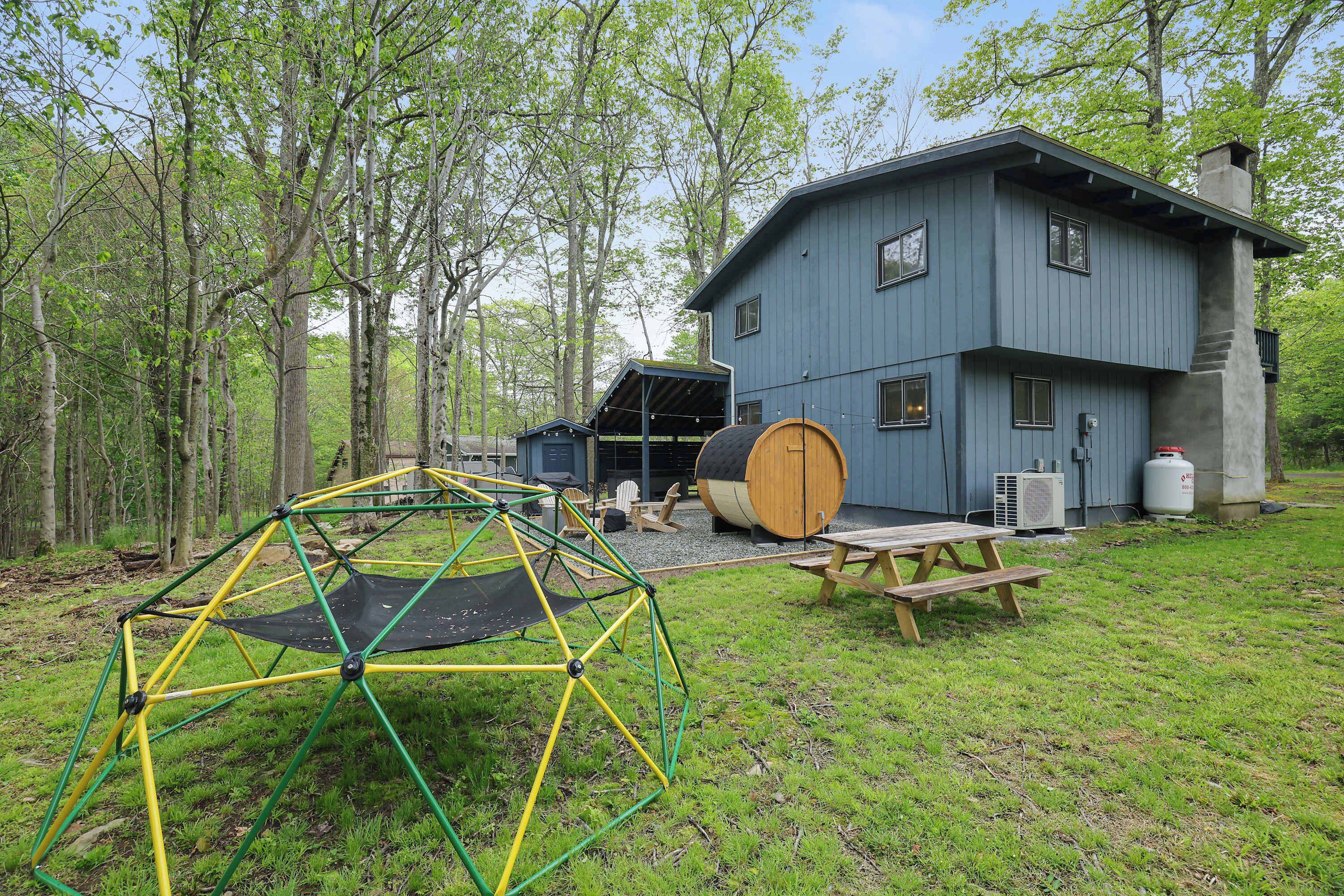 A blue house with a wooden deck, a trampoline, and picnic tables.