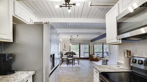 A modern kitchen with white cabinetry, a black stove, and a dining area with a table and chairs. - Bluewood Escape: Sauna, Hot Tub, Game Room (Tobyhanna)