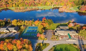 Vue aérienne d’un quartier résidentiel avec un court de tennis, un terrain de golf et une étendue d’eau.