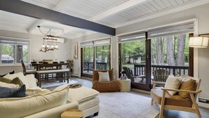 A spacious living room with a high ceiling, a dining area, and large windows offering a view of the outdoors. - Bluewood Escape: Sauna, Hot Tub, Game Room (Tobyhanna)
