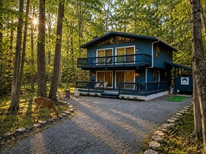 A two-story cabin with a balcony, surrounded by trees and a gravel path. - Bluewood Escape: Sauna, Hot Tub, Game Room (Tobyhanna)