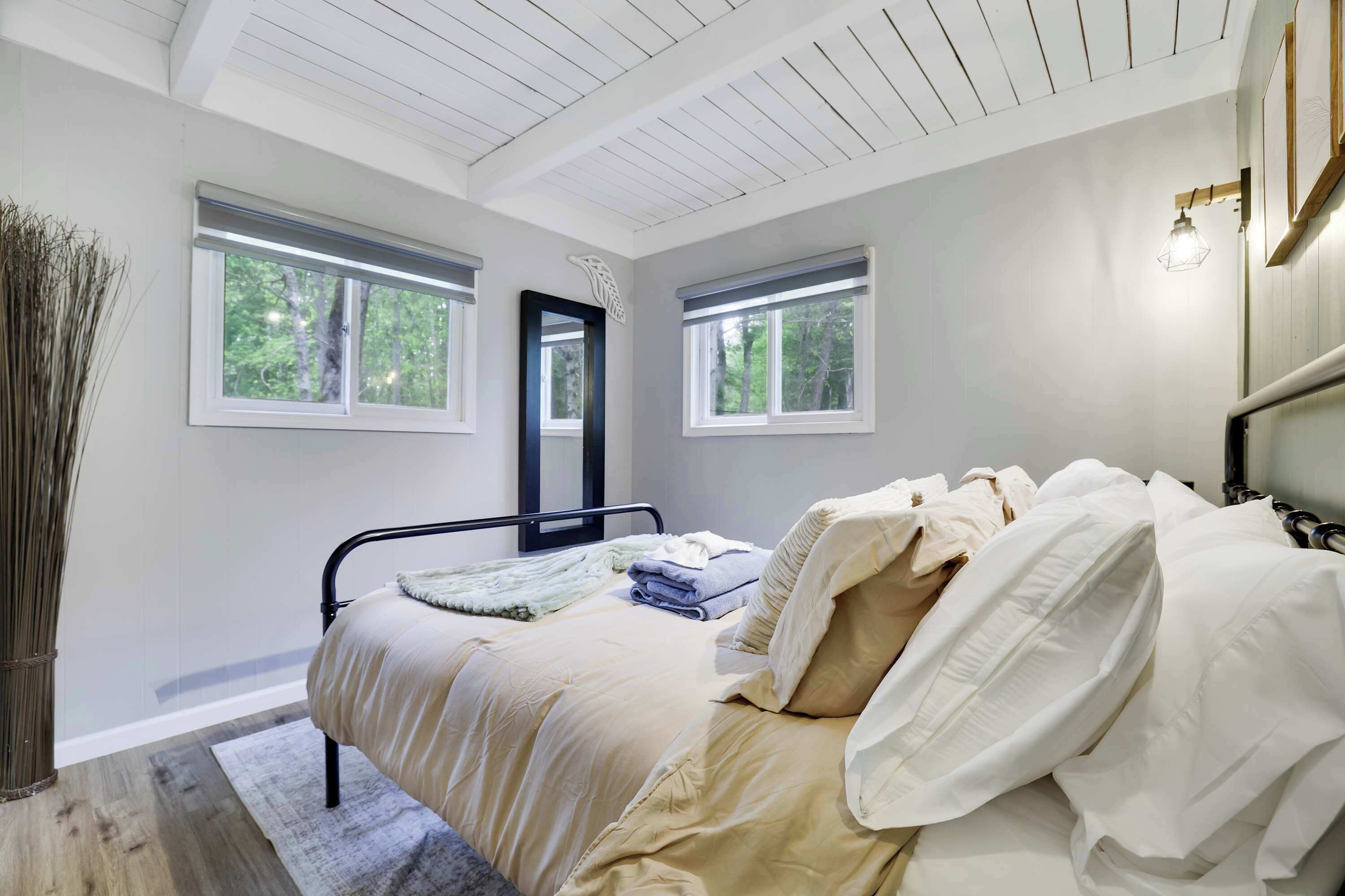 Ein Schlafzimmer mit einem Bett, zwei Fenstern, einem Spiegel und einer Lampe.