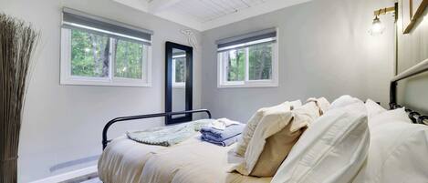 Ein Schlafzimmer mit einem Bett, zwei Fenstern, einem Spiegel und einer Lampe.