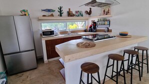 Eine moderne Küche mit einer zentralen Kochinsel, Barhocker, einem Kühlschrank und Dekoration an der Wand.