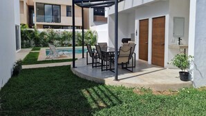 Eine überdachte Terrasse mit Pool, Sitzgelegenheiten im Freien und einem kleinen Garten.