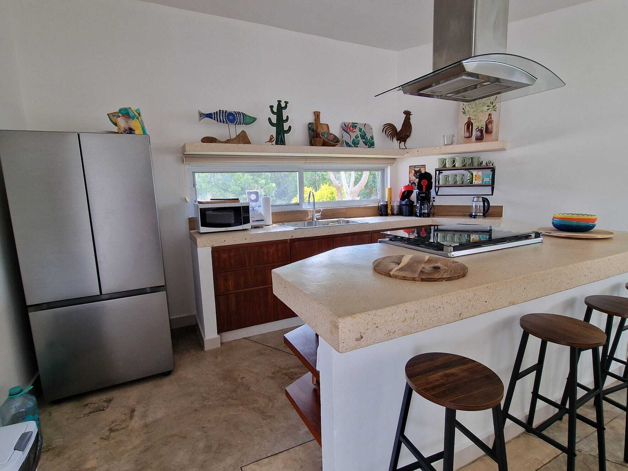 A modern kitchen with a stainless steel refrigerator, a microwave, and a large island with bar stools.