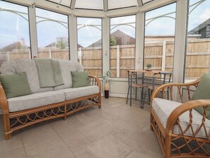 A conservatory with a wicker sofa, a dining table, and chairs. - Driftwood (Rhyl)