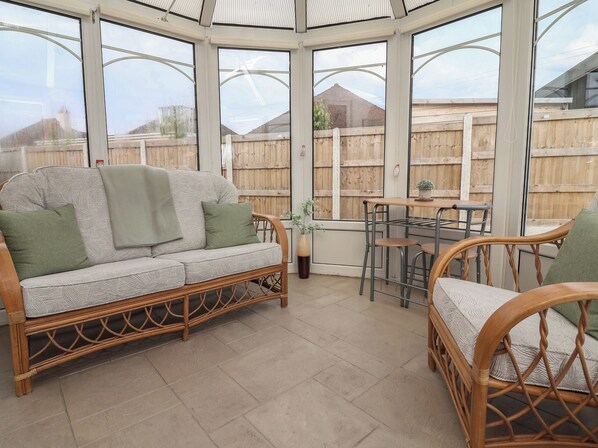 A conservatory with a wicker sofa, a dining table, and chairs. - Driftwood (Rhyl)