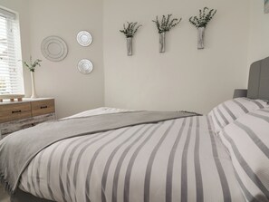 A bedroom with a bed, bedside tables, a dresser, and wall decorations including plates and vases. - Driftwood (Rhyl)