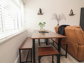 A dining area with a wooden table and benches, a brown sofa, and decorative wall art. - Driftwood (Rhyl)