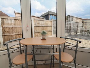 A corner room with a wooden table and metal chairs, a small potted plant, and a view of a wooden fence and building outside. - Driftwood (Rhyl)