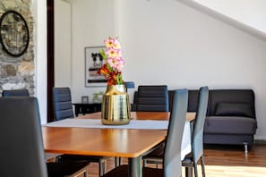 Uma mesa de jantar com um vaso de flores, rodeada por cadeiras, em um quarto moderno com parede de pedra e um sofá.