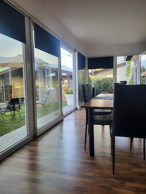 A modern room with large sliding glass doors, a wooden floor, and a dining area with chairs.