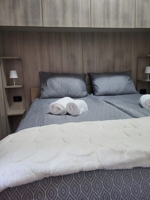 A neatly made bed with rolled towels, a patterned bedspread, and a wooden headboard.