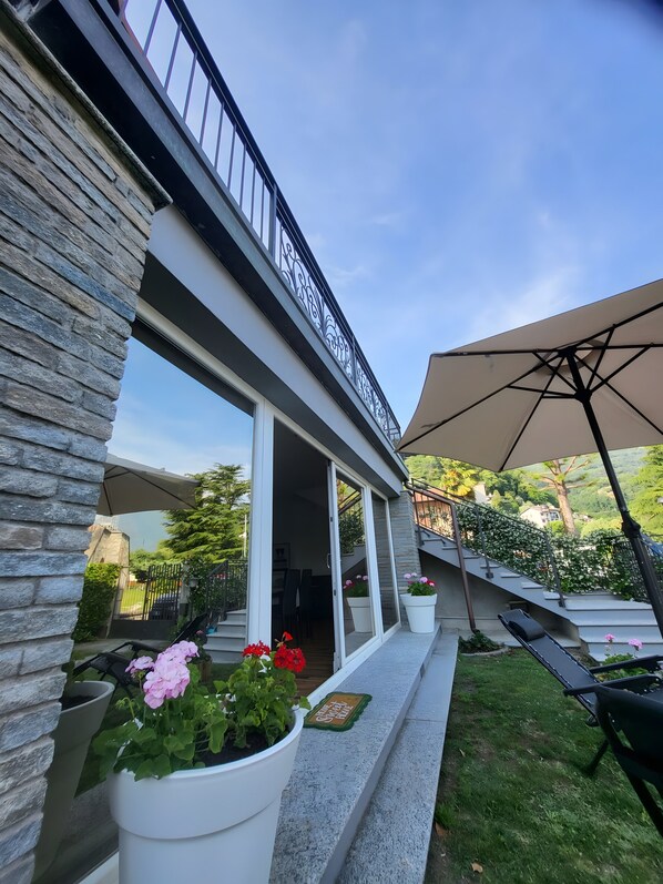 A modern building with a stone facade, large windows, and a balcony with outdoor seating.