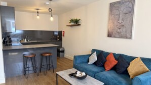 Eine moderne Küche mit Barbereich, ein blaues Sofa mit Kissen und ein minimalistisches Kunstwerk an der Wand.