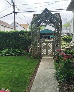 Un jardin agrémenté d’une tonnelle en bois et d’un chemin en béton.