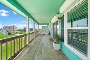 Eine überdachte Veranda mit Holzterrasse, Blumentöpfen und Blick auf benachbarte Häuser.