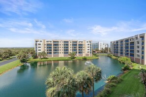 A multi-story hotel with a central courtyard, palm trees, and a body of water. - Oceanwalk 15-403 (New Smyrna Beach)