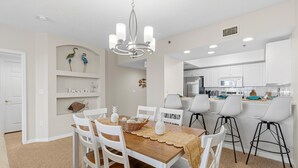 A dining area with a wooden table, white chairs, and a chandelier. - Oceanwalk 15-403 (New Smyrna Beach)