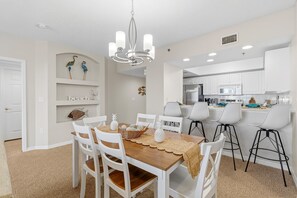 A dining area with a wooden table, white chairs, and a chandelier. - Oceanwalk 15-403 (New Smyrna Beach)