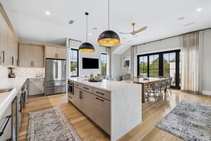 A modern kitchen with a central island, stainless steel appliances, and a dining area with a large window. - Casa Amor|Easy Beach Access|Private Pool|Golf Cart (Seagrove Beach)