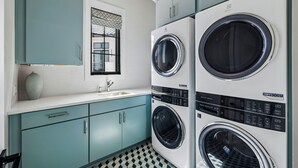 Una sala de lavandería con dos lavadoras de carga frontal, un lavabo y gabinetes color turquesa.