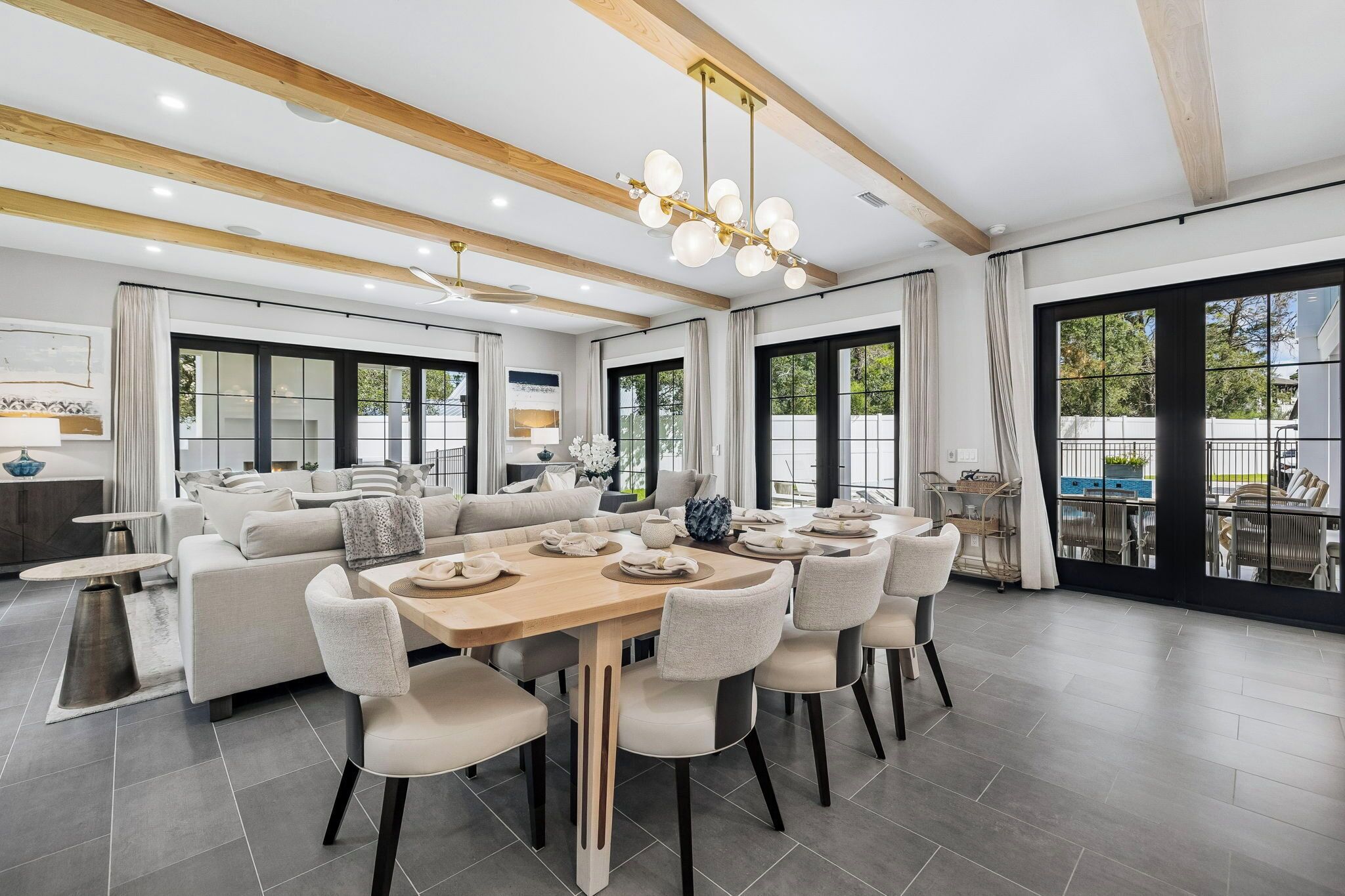 A modern dining area with a wooden table and chairs, large windows, and a ceiling fan.