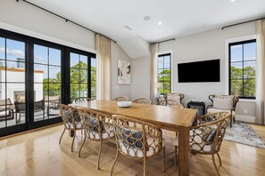 A spacious dining area with a long wooden table, wicker chairs with cushions, and large windows offering a view of the outdoors. - Casa Amor|Easy Beach Access|Private Pool|Golf Cart (Seagrove Beach)