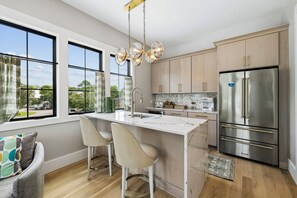 A modern kitchen with a central island, stainless steel appliances, and large windows offering a view of the outdoors. - Casa Amor|Easy Beach Access|Private Pool|Golf Cart (Seagrove Beach)