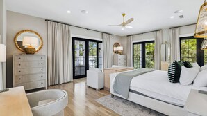 Un dormitorio moderno con una cama grande, un escritorio, una silla y un aparador. Tiene un balcón con vistas a la vegetación.