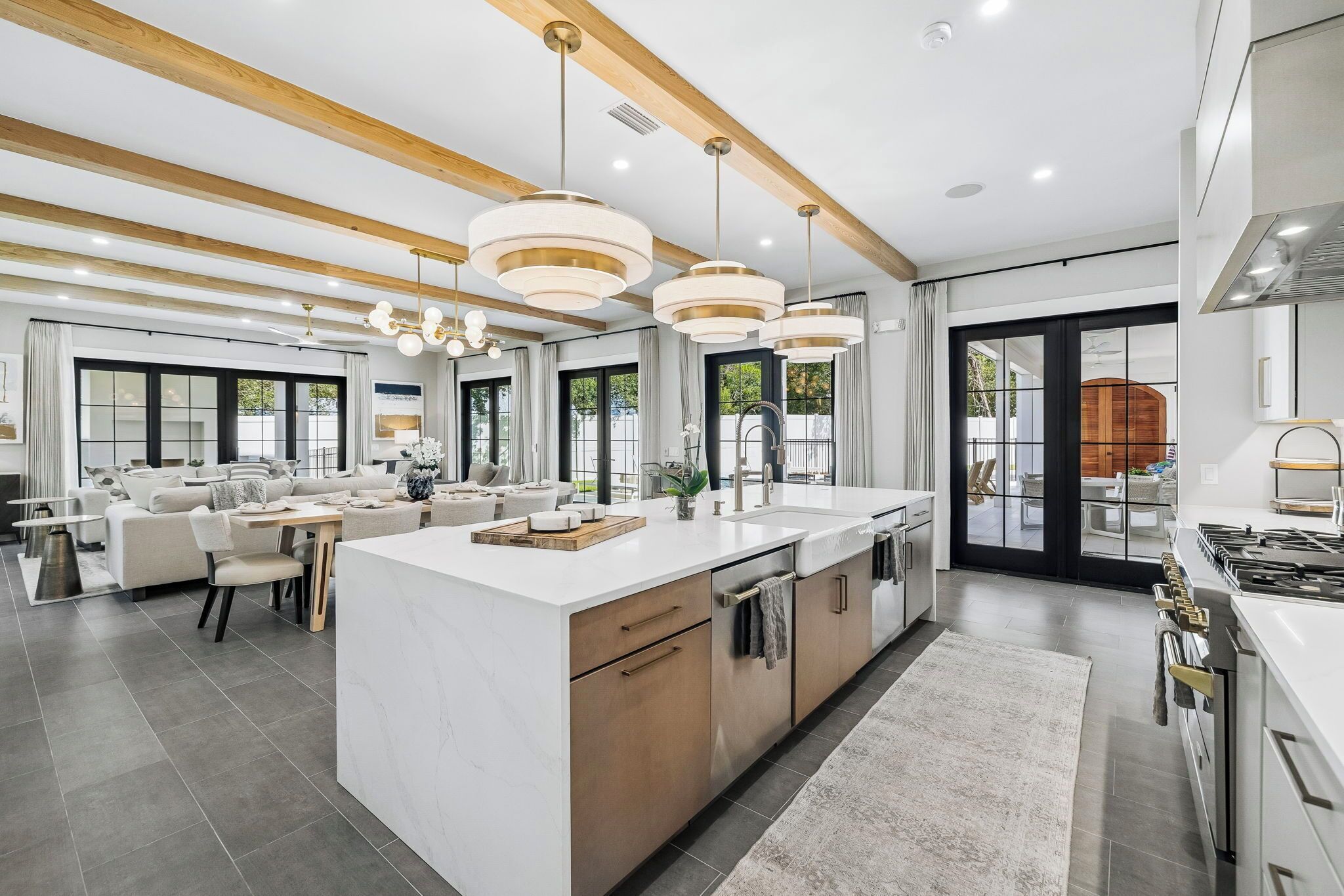 A modern kitchen with a large island, pendant lighting, and a view to the outdoor area.