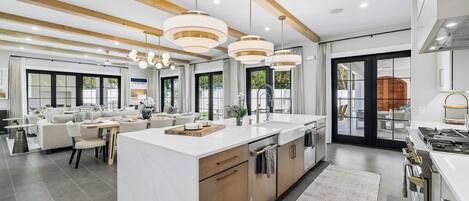 A modern kitchen with a large island, pendant lighting, and a view to the outdoor area.