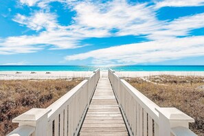 Ein aus Holz gefertigter Steg, der zu einem Strand mit blauem Himmel führt.