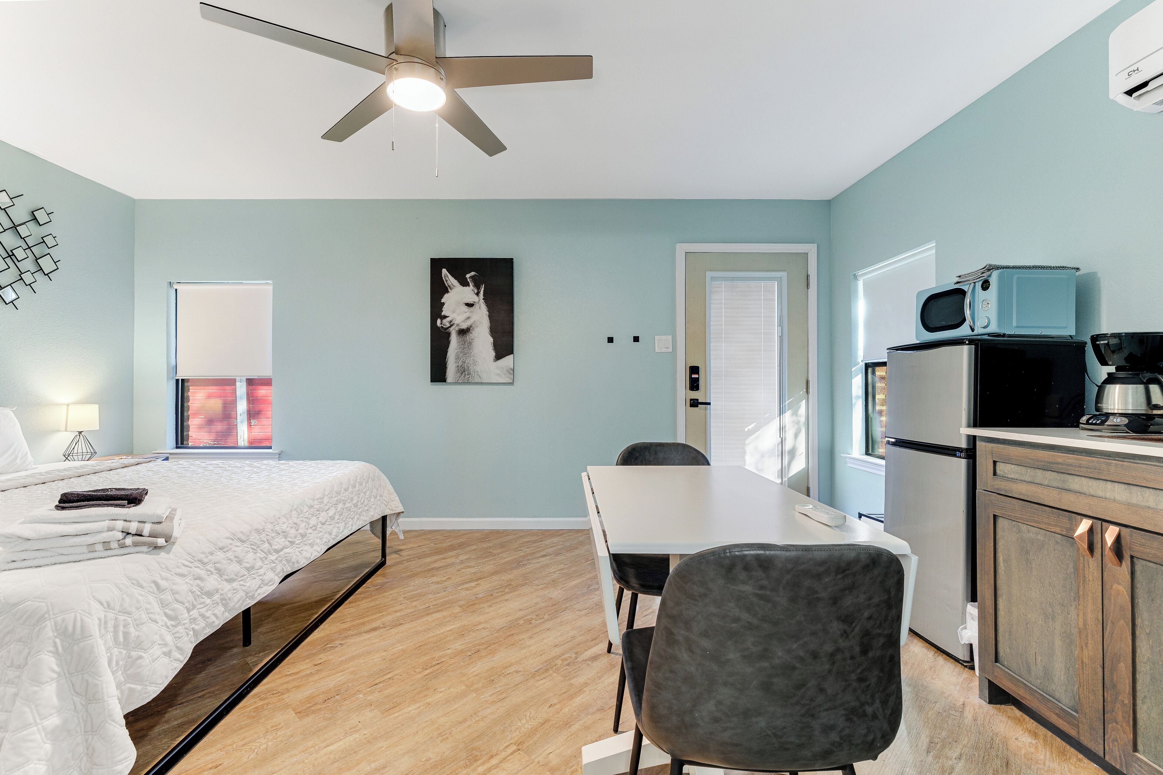 A bedroom with a bed, a desk, a chair, a ceiling fan, a microwave, and a refrigerator.