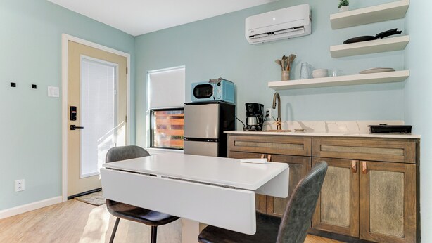 Una cocina moderna con una mesa blanca, un refrigerador, un microondas y armarios de madera.