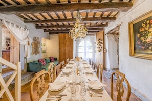 Ein Esszimmer mit langem Tisch, gedeckt für eine Mahlzeit, Holzbalken an der Decke und einem Kronleuchter.