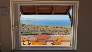 Ein Balkon mit Tisch und Stühlen, der auf eine Küstenlandschaft mit Gebäuden und dem Meer blickt.