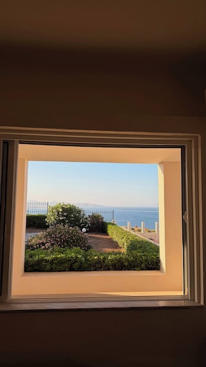 Una finestra con vista su un giardino e il mare.