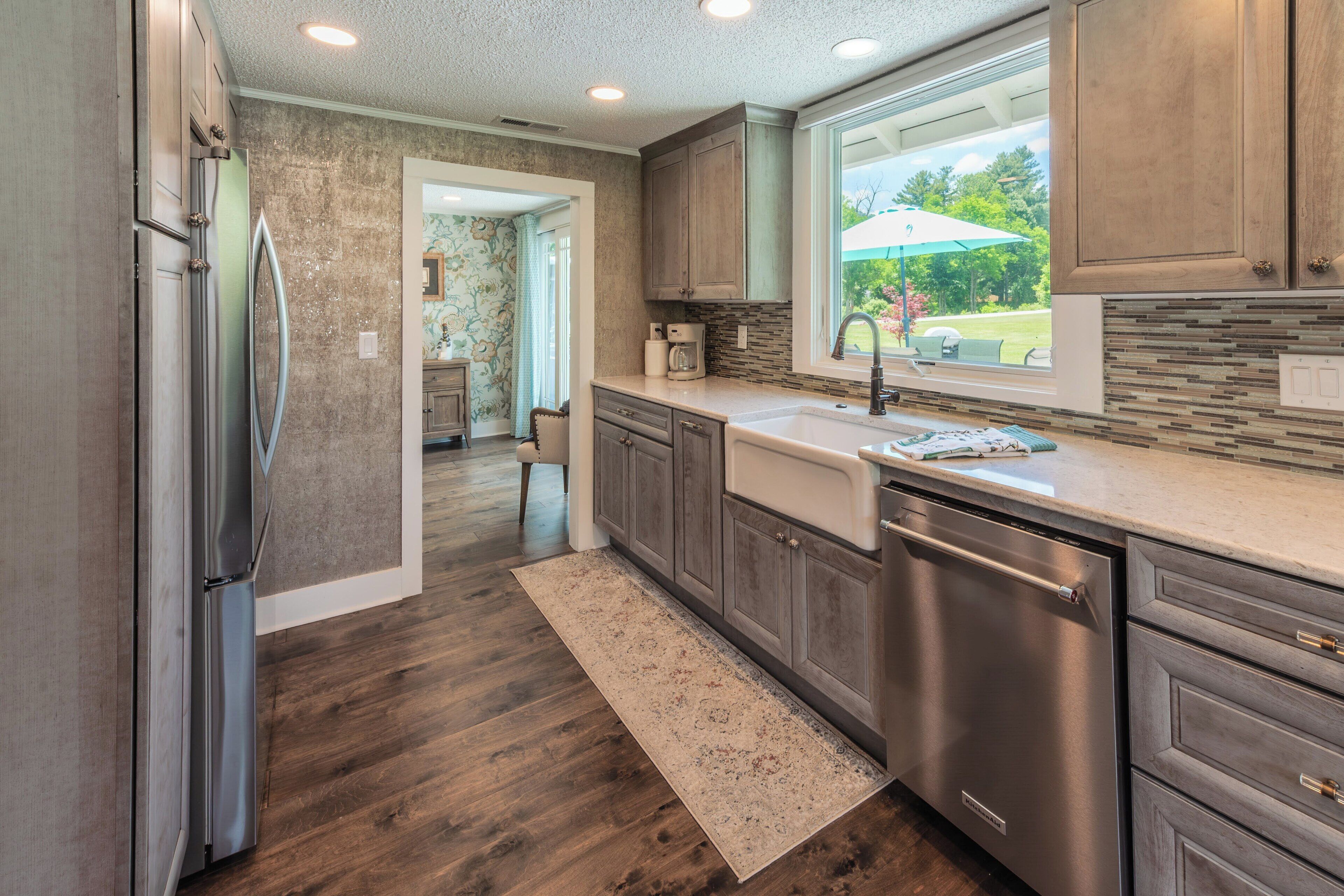 A modern kitchen with wooden cabinets, stainless steel appliances, a large window, and a view of the outdoors.