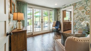 Ein Zimmer mit Holzschrank, Lampe, Stuhl, Sofa und Blick auf eine Terrasse durch Glastüren.