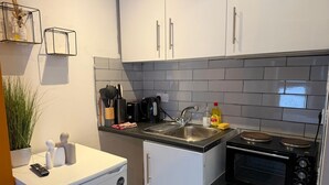 Een kleine keuken met witte kastjes, een zwart aanrecht, een spoelbak, een koffiezetapparaat, een broodrooster en een magnetron.