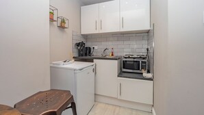 Een compacte keuken met witte kastjes, een magnetron, een koffiezetapparaat en een klein aanrecht.
