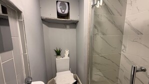Een badkamer met toilet, douche en handdroger op een plank.