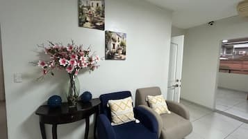 A living room with a sofa, armchairs, a small table with a vase of flowers, and two wall-mounted pictures.